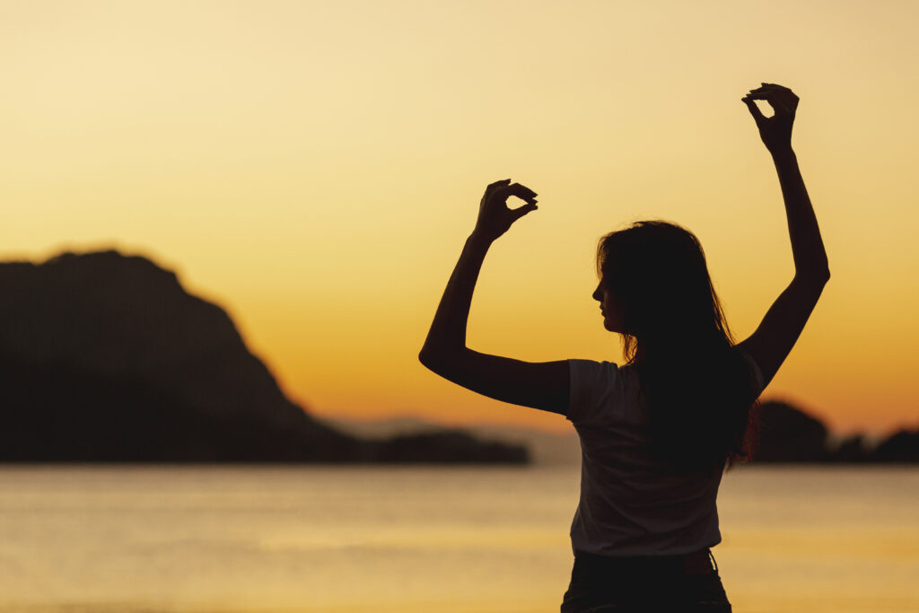 Silhouette of a woman practicing mindful movement at sunset near a serene body of water, symbolizing inner peace and personal power