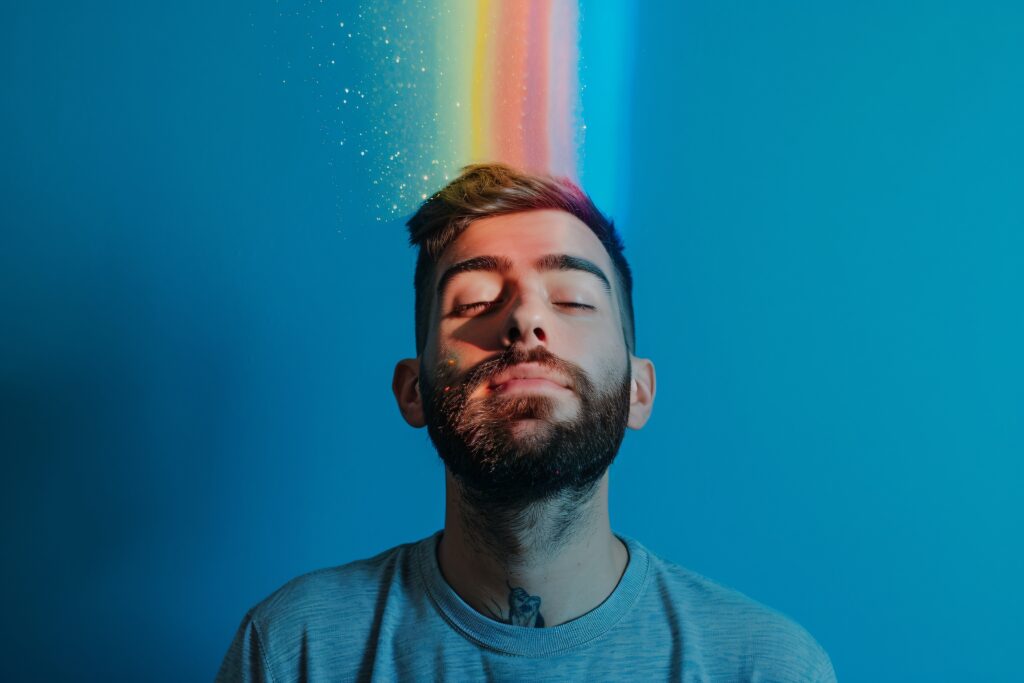  A person with closed eyes and a peaceful expression, with rainbow colors symbolizing elevated thoughts and energy radiating from their head, illustrating the concept of how to raise your vibration.