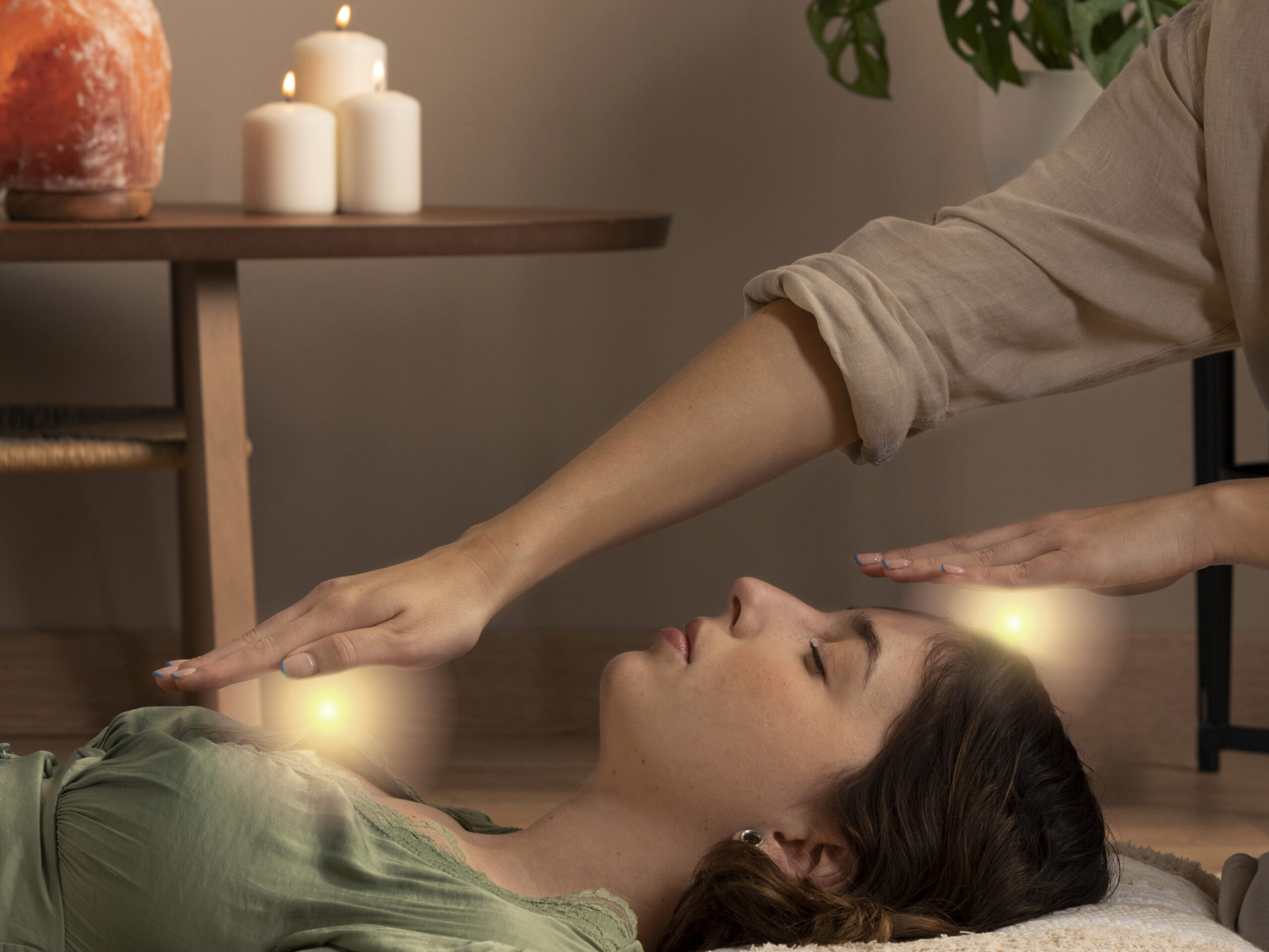 Therapist performing energy healing on a woman lying down in a peaceful setting with candles and plants, symbolizing spiritual growth and healing