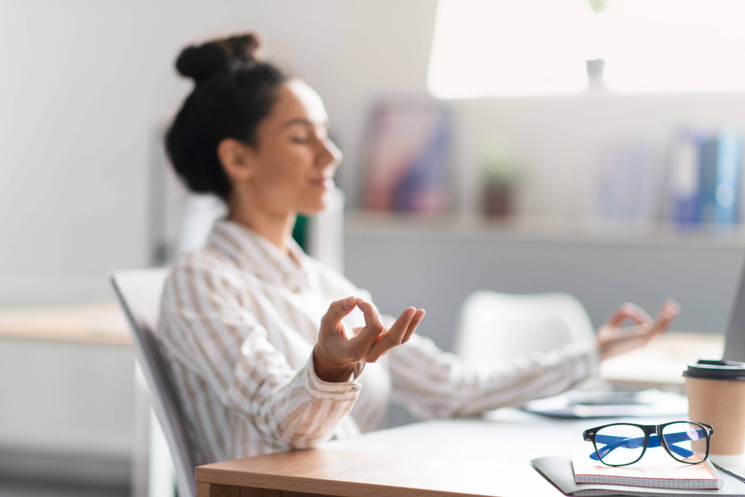 A female entrepreneur meditating at her desk, managing workplace stress through conscious business practices.