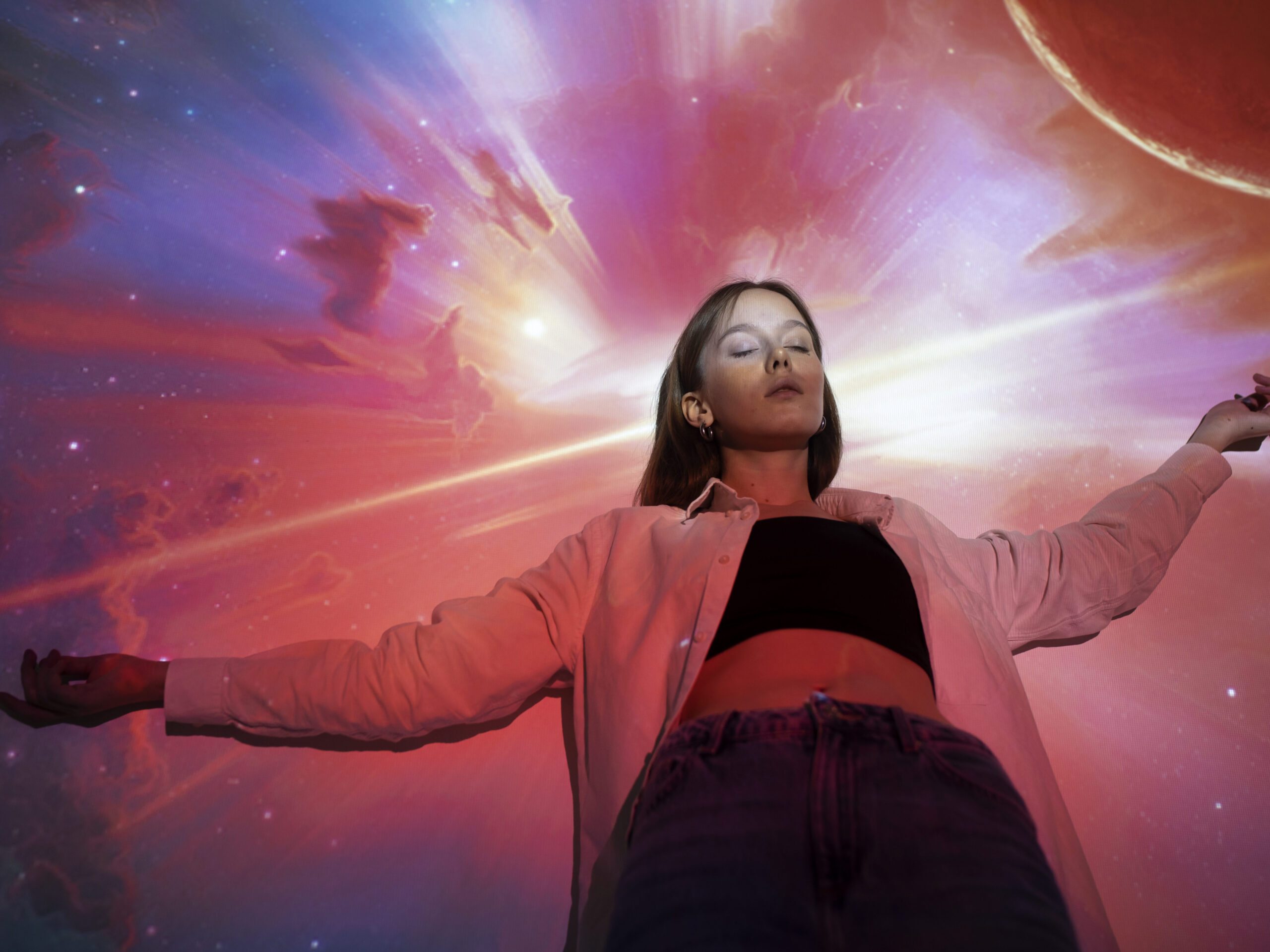 Young woman standing with eyes closed and arms outstretched, illuminated by a cosmic background with vibrant colors, symbolizing law of attraction and connection to the universe