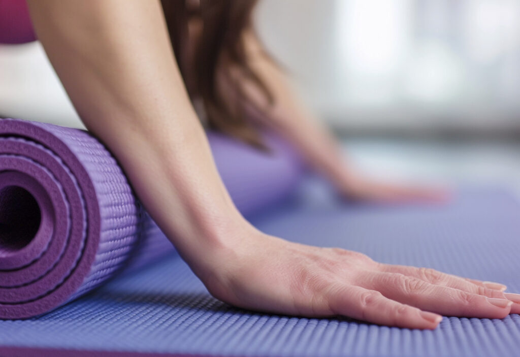 Close-up of a person rolling out a purple yoga mat, preparing for a yoga session, symbolizing readiness and mindfulness in practice