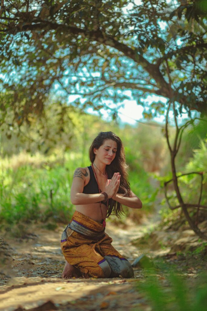 A woman kneels in a meditative pose under a tree in a sunny outdoor setting looking inwards to counter new age deception