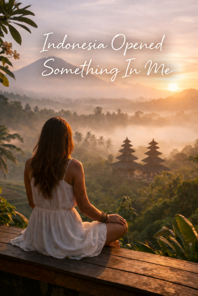 Woman in a white dress sitting on a wooden ledge at sunrise, overlooking misty Balinese jungle and temple rooftops, with the words ‘Indonesia Opened Something In Me’ written across the sky
