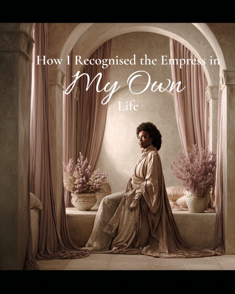 A woman seated beneath soft stone arches and flowing curtains, wearing a draped gown and gazing calmly forward, symbolising recognising the Empress archetype through lived experience, grounded confidence, and embodied feminine authority.
